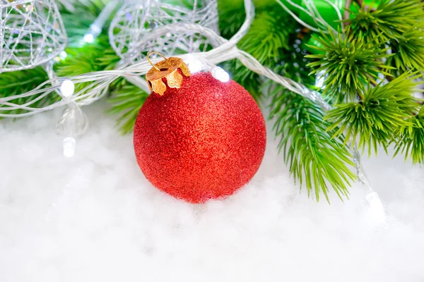 Weihnachtsdekoration mit roter Kugel, grünem Tannenzweig und weißen Lichtern im Schnee. Grußkarte — Stockfoto
