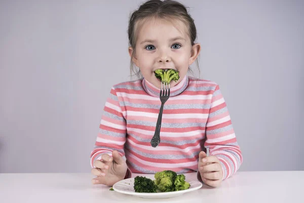 포크를 사용하여 브로콜리를 먹고 있는 웃긴 어린 소녀 — 스톡 사진