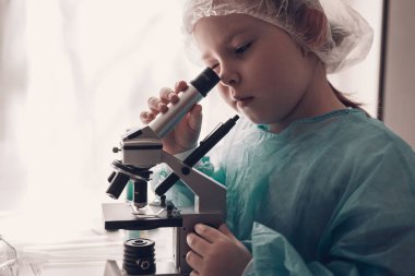 Laboratuvarda laboratuvar önlüklü küçük kız kimya öğreniyor. Koruyucu gözlüklü genç bilim adamı laboratuvar ya da kimya dolabında deney yapıyor. Mikroskoptan bakıyorum.. 