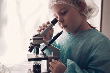 Laboratuvarda laboratuvar önlüklü küçük kız kimya öğreniyor. Koruyucu gözlüklü genç bilim adamı laboratuvar ya da kimya dolabında deney yapıyor. Mikroskoptan bakıyorum.. 