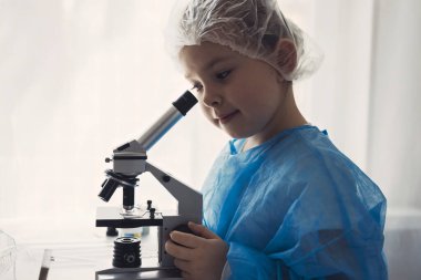 Laboratuvarda laboratuvar önlüklü küçük kız kimya öğreniyor. Koruyucu gözlüklü genç bilim adamı laboratuvar ya da kimya dolabında deney yapıyor. Mikroskoptan bakıyorum.. 