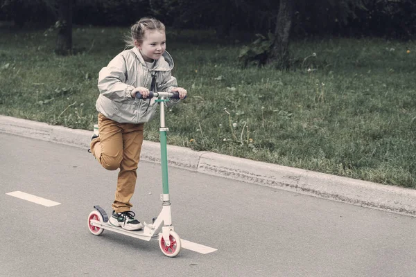 Portret van actieve kleine peuter meisje paardrijden scooter op de weg in het park buiten op zomerdag. Seizoensgebonden sport voor kinderen. — Stockfoto