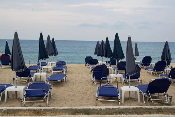 Cadeiras vazias sob guarda-chuvas de palha em uma praia de areia — Fotografia de Stock