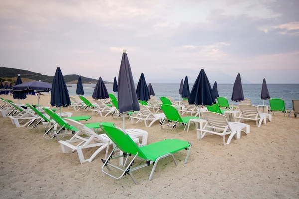 Sillas vacías bajo sombrillas de paja en una playa de arena —  Fotos de Stock