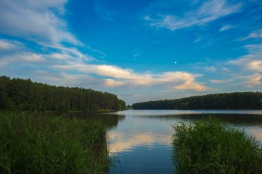 Gün batımında dinlenen göl, sakin bir yaz akşamında gölün üzerinde renkli günbatımı. Göl üzerindeki gökyüzünün yansıması gün batımına dramatik bir etki yaptı.