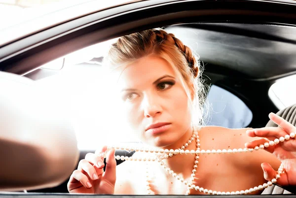 真珠のネックレスで若い女性が彼女の c の運転席に座ってください。 — ストック写真