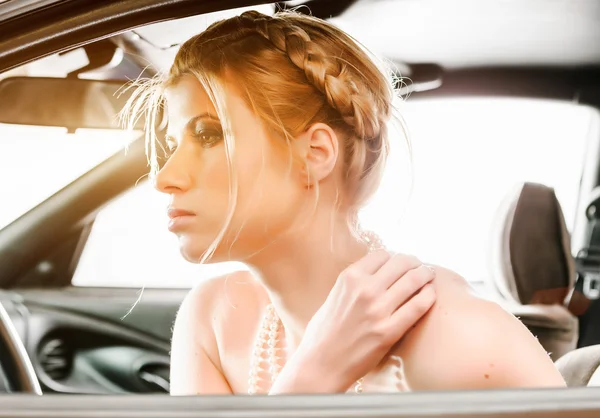 Mujer joven en un collar de perlas sentado en el asiento de los conductores de su c — Foto de Stock