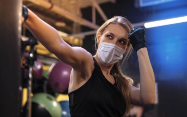 Salgın sırasında yüz maskeli genç bir kadın spor salonunda çalışıyor.