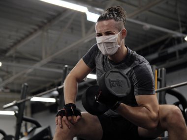 Salgın sırasında yüz maskeli genç bir adam spor salonunda çalışıyor.