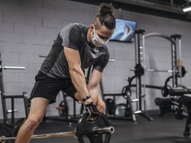 Salgın sırasında yüz maskeli genç bir adam spor salonunda çalışıyor.
