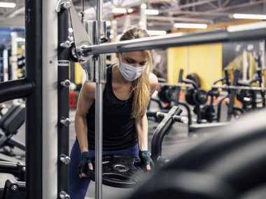 Salgın sırasında yüz maskeli genç bir kadın spor salonunda çalışıyor.