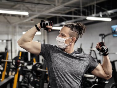 Genç bir adam yüz maskesi takıyor ve salgın sırasında spor salonunda çalışıyor.