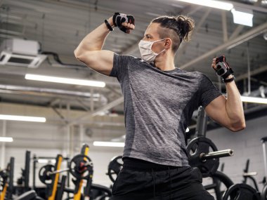 Genç bir adam yüz maskesi takıyor ve salgın sırasında spor salonunda çalışıyor.