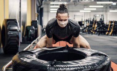 Genç bir adam yüz maskesi takıyor ve salgın sırasında spor salonunda çalışıyor.