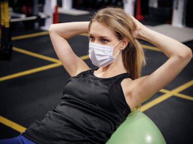 Genç bir kadın güvenlik maskesi takıyor ve spor salonunda çalışıyor.