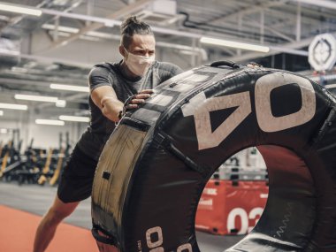 Genç bir adam yüz maskesi takıyor ve salgın sırasında spor salonunda çalışıyor.