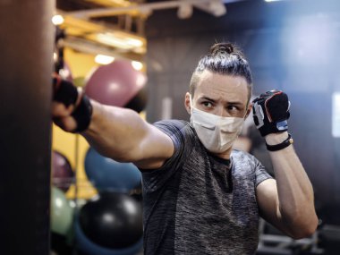 Genç bir adam yüz maskesi takıyor ve salgın sırasında spor salonunda çalışıyor.