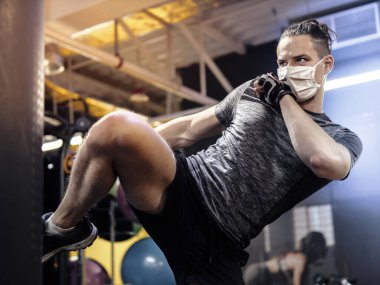 Genç bir adam yüz maskesi takıyor ve salgın sırasında spor salonunda çalışıyor.