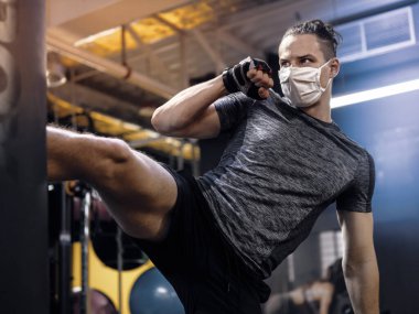 Genç bir adam yüz maskesi takıyor ve salgın sırasında spor salonunda çalışıyor.