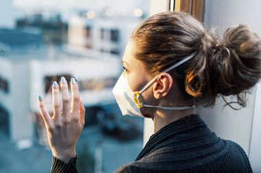 Hava kirliliği sırasında karantina, virüs salgını, evde ya da hastanede tecrit. Kadın pencereden dışarı doğru bakıyor. Bir kadın yüz maskesi takıyor..