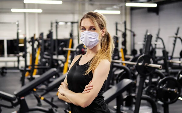 Spor salonunda maske takan genç bir kadın.