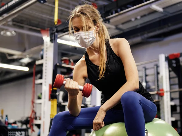Genç bir kadın güvenlik maskesi takıyor ve spor salonunda çalışıyor.