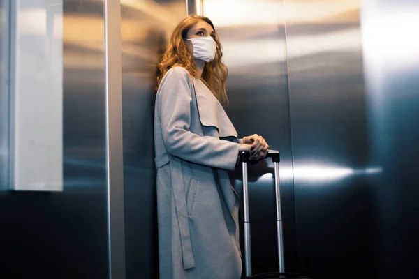 A young woman with a luggage is wearing safety mask in an elevator