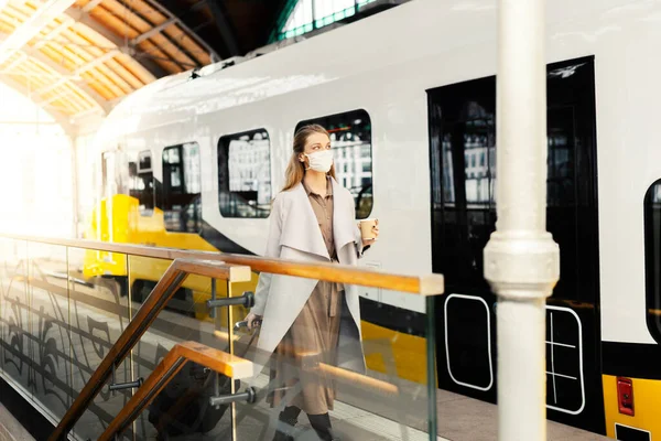 A young woman with a luggage is wearing a safety mask while using the public transportation