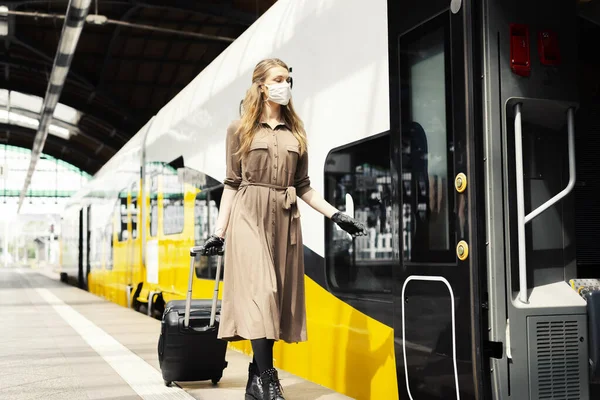 A young woman with a luggage is wearing a safety mask while using the public transportation