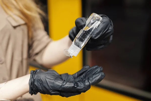 A young woman in a safety mask and gloves is using an antibacterial sanitizer in public transportation in a pandemic outbreak