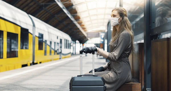 A young woman with a luggage is wearing a safety mask while using the public transportation