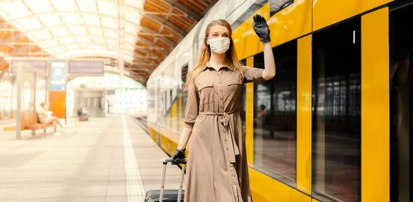 A young woman with a luggage is wearing a safety mask while using the public transportation