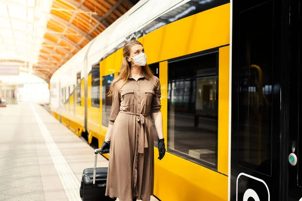 A young woman with a luggage is wearing a safety mask while using the public transportation