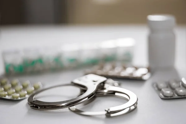 Kelepçeler, haplar ve uyuşturucular beyaz masada. Seçici odak