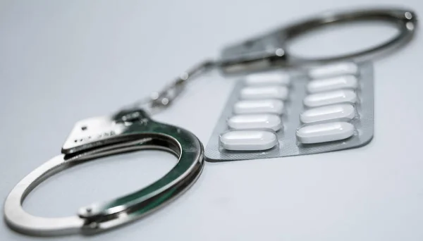 Handcuffs and pills and drugs on white table. — Stock Photo, Image