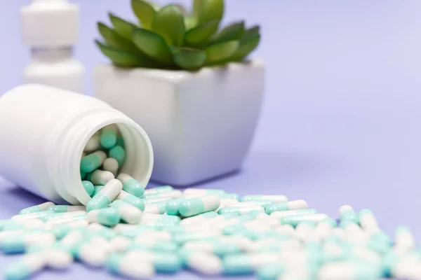 Blue and white capsules pill spilled out from white plastic bottle container. Global healthcare concept. Antibiotics drug resistance. Antimicrobial capsule pills. Pharmaceutical industry. Pharmacy.