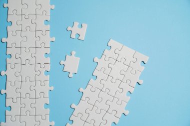 Kayıp yapboz parçaları. İş konsepti. Katlanmış beyaz yapboz parçası ve mavi bir yüzeyin arka planına karşı taranmamış bir yığın yapboz..