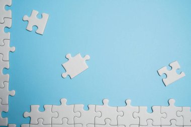 Kayıp yapboz parçaları. İş konsepti. Katlanmış beyaz yapboz parçası ve mavi bir yüzeyin arka planına karşı taranmamış bir yığın yapboz..