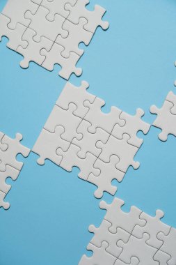 Kayıp yapboz parçaları. İş konsepti. Katlanmış beyaz yapboz parçası ve mavi bir yüzeyin arka planına karşı taranmamış bir yığın yapboz..