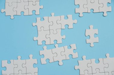 Kayıp yapboz parçaları. İş konsepti. Katlanmış beyaz yapboz parçası ve mavi bir yüzeyin arka planına karşı taranmamış bir yığın yapboz..