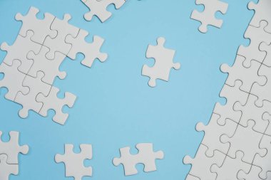 Kayıp yapboz parçaları. İş konsepti. Katlanmış beyaz yapboz parçası ve mavi bir yüzeyin arka planına karşı taranmamış bir yığın yapboz..
