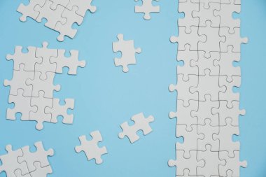 Kayıp yapboz parçaları. İş konsepti. Katlanmış beyaz yapboz parçası ve mavi bir yüzeyin arka planına karşı taranmamış bir yığın yapboz..