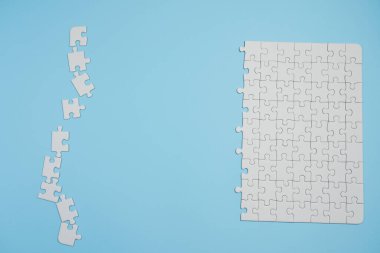 Kayıp yapboz parçaları. İş konsepti. Katlanmış beyaz yapboz parçası ve mavi bir yüzeyin arka planına karşı taranmamış bir yığın yapboz..