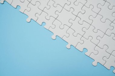 Kayıp yapboz parçaları. İş konsepti. Katlanmış beyaz yapboz parçası ve mavi bir yüzeyin arka planına karşı taranmamış bir yığın yapboz..