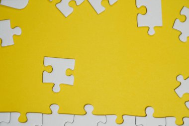 Kayıp yapboz parçaları. İş konsepti. Katlanmış beyaz yapboz parçası ve sarı bir yüzeyin arka planında taranmamış bir yığın yapboz..