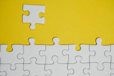 Kayıp yapboz parçaları. İş konsepti. Katlanmış beyaz yapboz parçası ve sarı bir yüzeyin arka planında taranmamış bir yığın yapboz..