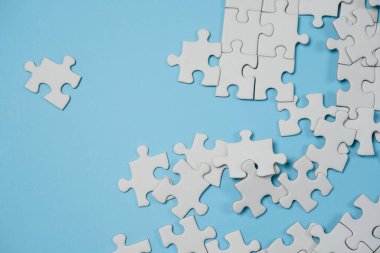 Kayıp yapboz parçaları. İş konsepti. Katlanmış beyaz yapboz parçası ve mavi bir yüzeyin arka planına karşı taranmamış bir yığın yapboz..