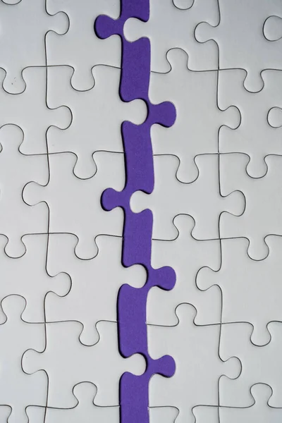 Missing jigsaw puzzle pieces. Business concept. Fragment of a folded white jigsaw puzzle and a pile of uncombed puzzle elements against the background of a Violet surface.