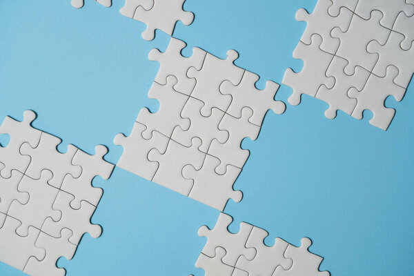 Missing jigsaw puzzle pieces. Business concept. Fragment of a folded white jigsaw puzzle and a pile of uncombed puzzle elements against the background of a blue surface.