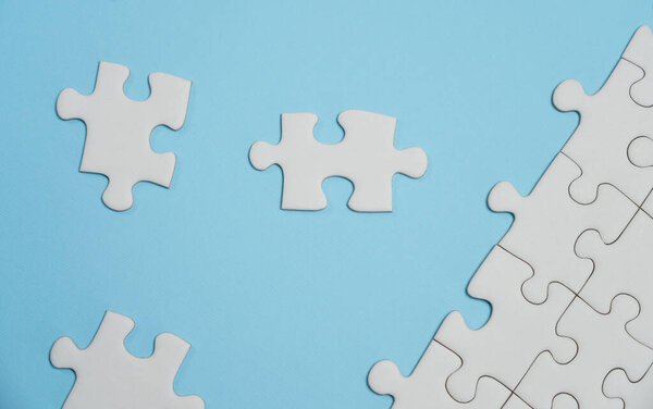 Missing jigsaw puzzle pieces. Business concept. Fragment of a folded white jigsaw puzzle and a pile of uncombed puzzle elements against the background of a blue surface.